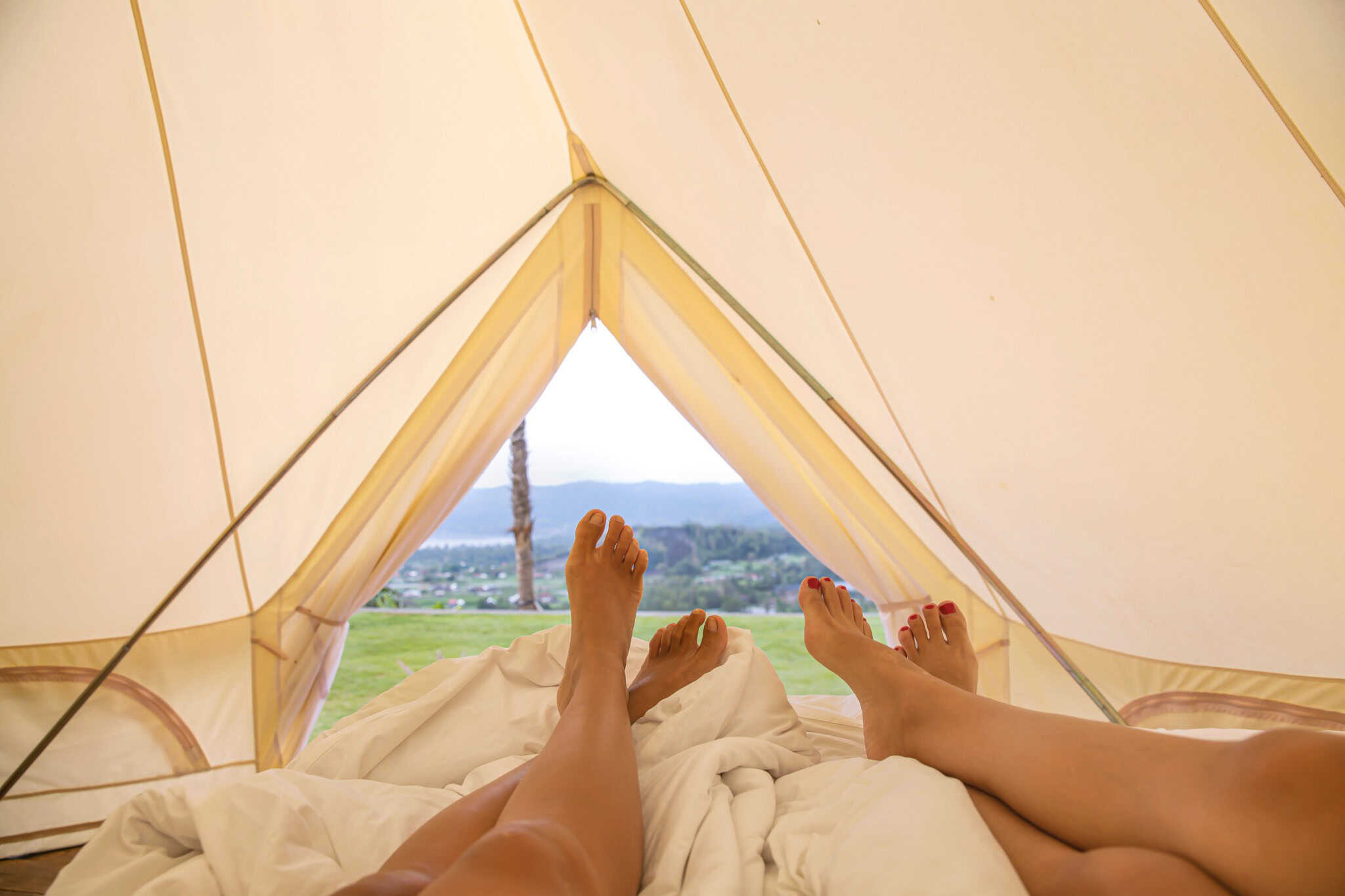 pair-of-bare-legs-and-feet-on-bed-inside-bell-tent-looking-out-on-a-sunny-day